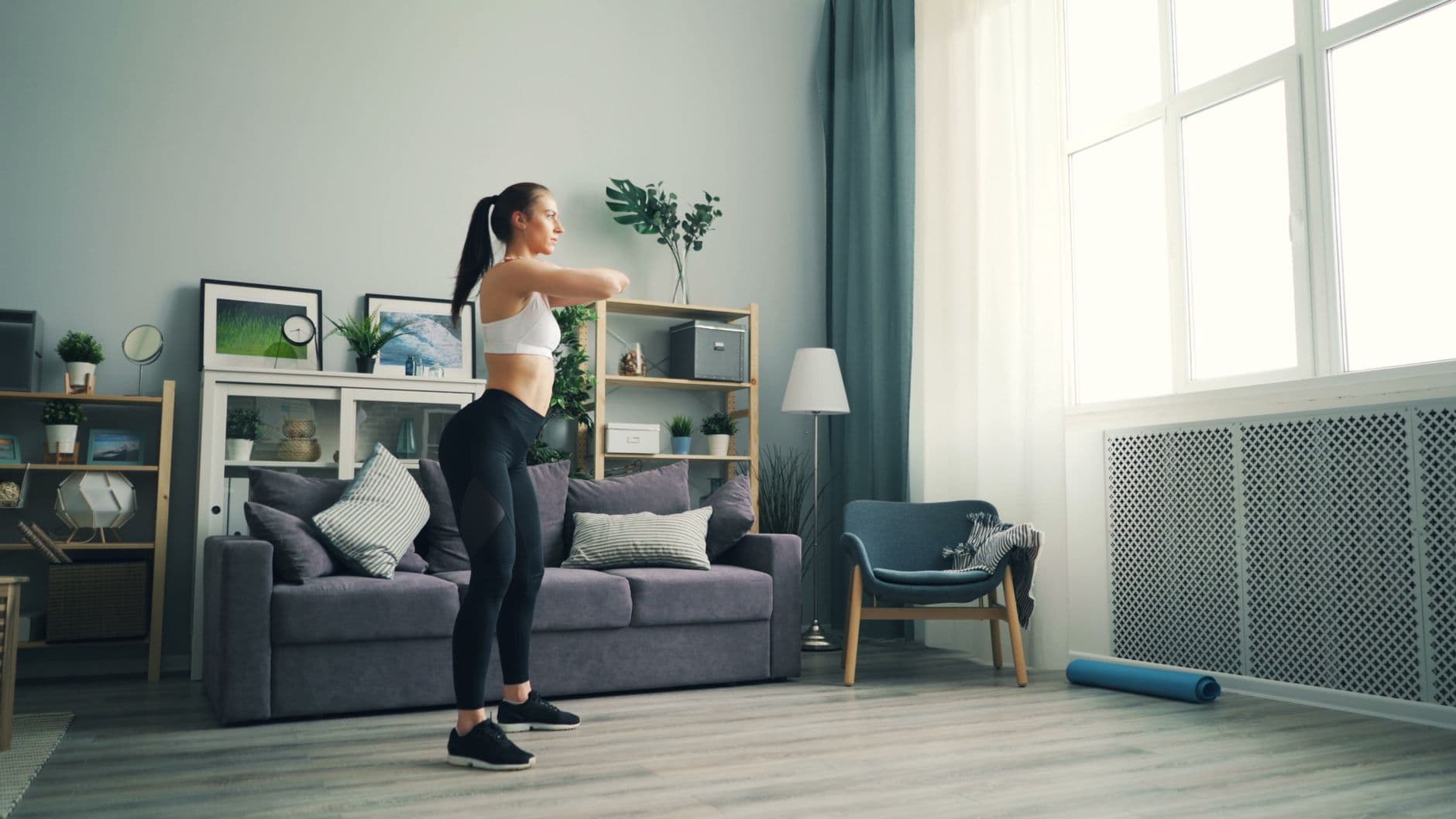 Kobieta w sportowym stroju wykonuje świadomy trening siłowy w domowym salonie, skupiając się na poprawnej technice przysiadu.