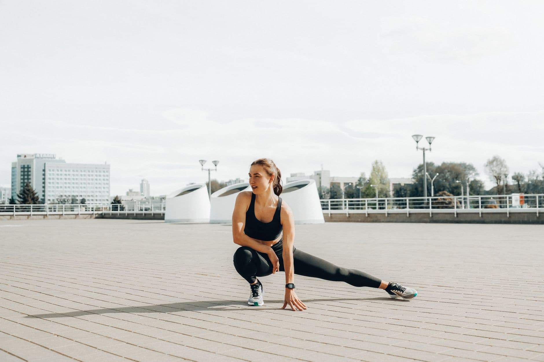 Kobieta w stroju sportowym wykonująca poprawny technicznie przysiad z własnym ciężarem ciała w słonecznym, przytulnym salonie jako element treningu siłowego w domu.